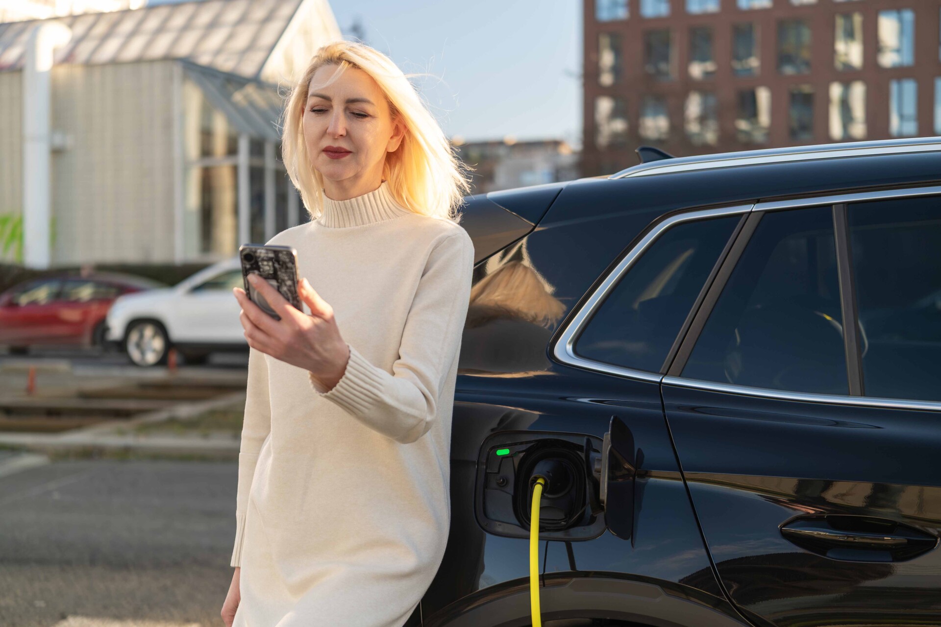 Woman using smartphone while charging her electric 2026 05 20 15 02 31 utc lr